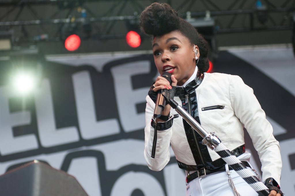 Janelle Monae sings into a silver microphone wearing a black and white outfit