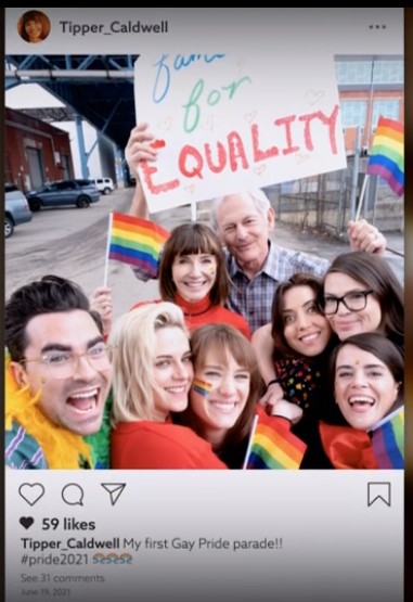 A screenshot of a mockup instagram post from the Happiest Season credits, showing the entire main cast waving rainbow flags plus director Clea DuVall, who has her arm around Aubrey Plaza.