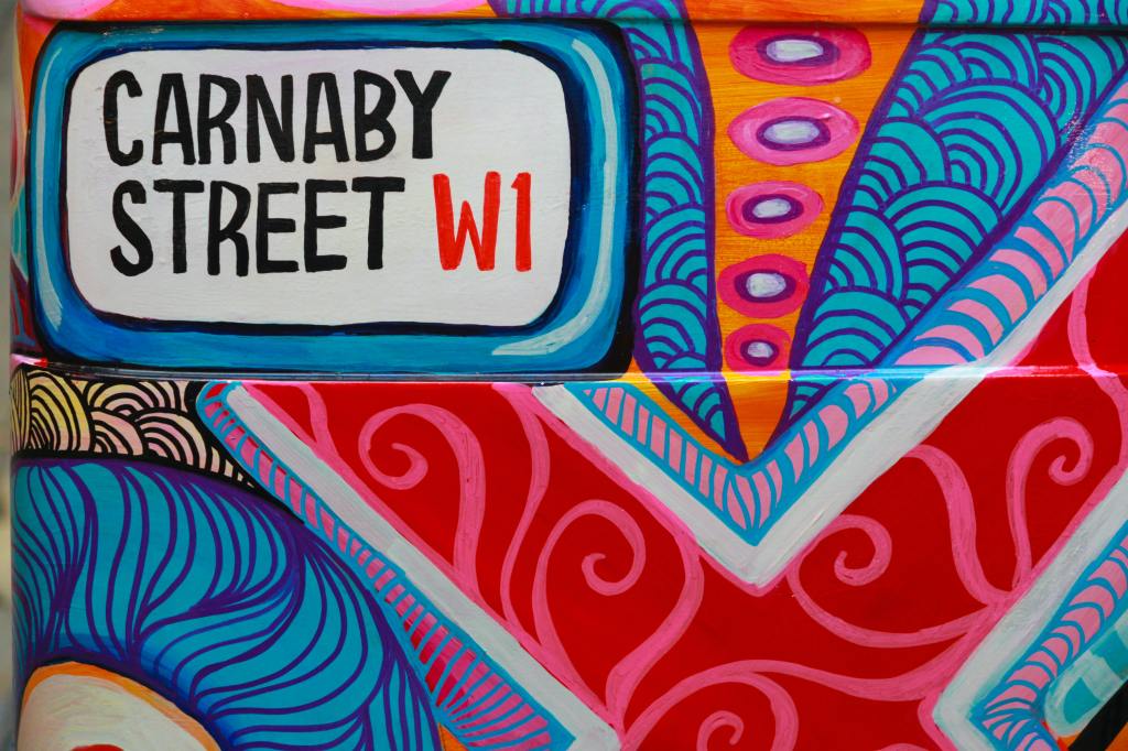 A wall painted in colourful stripes, swirls and patterns, with a block at the top left reading "Carnaby Street W1"
